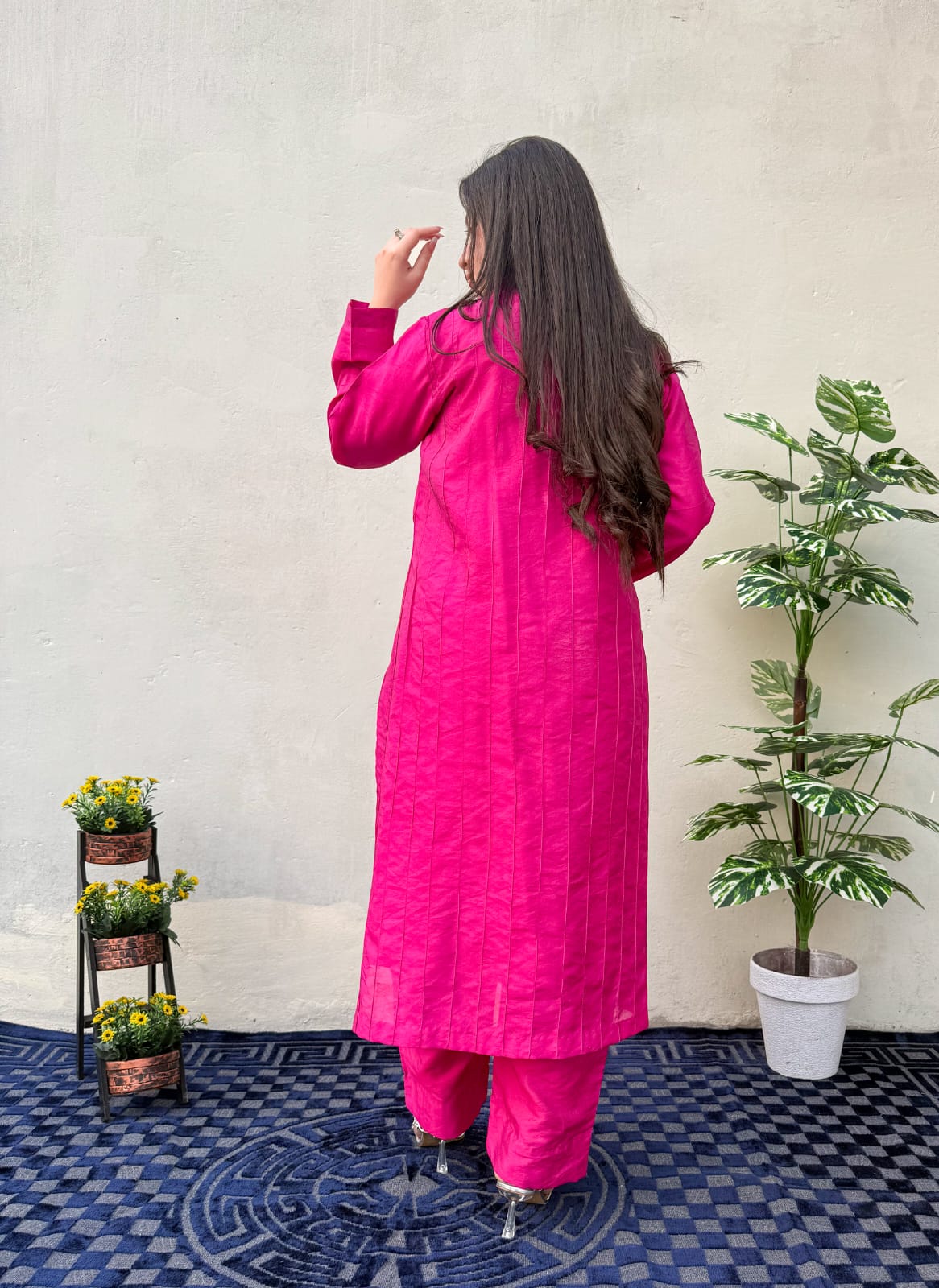 Woman in a bright pink traditional outfit standing in front of a white wall with plants