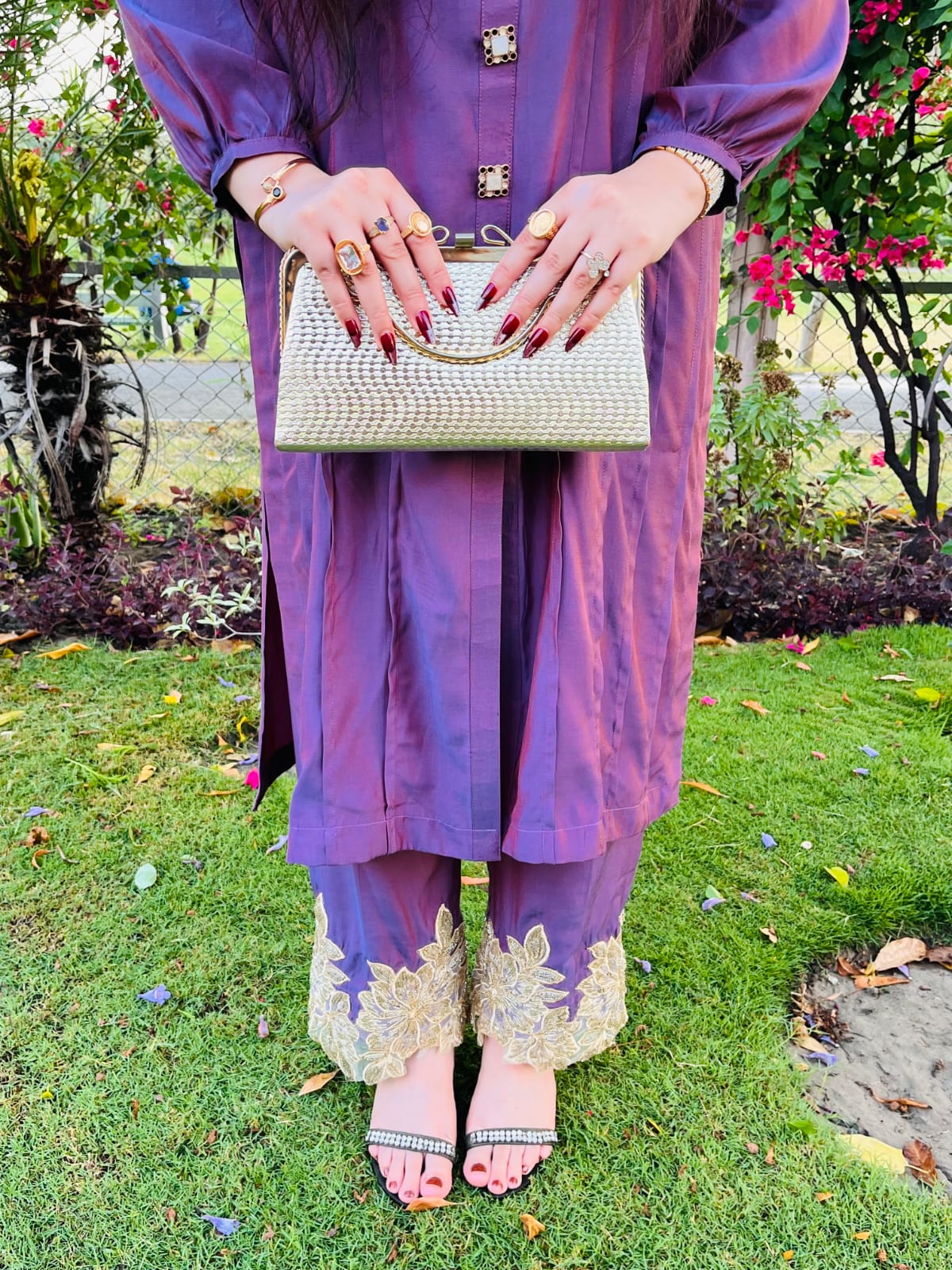 Girl wearing a purple outfit with gold embroidery, holding a white handbag in an outdoor setting