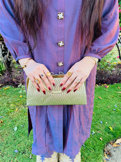 Girl wearing a purple outfit with gold buttons, holding a gold clutch against a green outdoor background